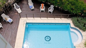 Ein rechteckiger Pool mit einem Logo in der Mitte, umgeben von einer Holzterrasse mit Liegestühlen.