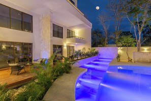 A modern house with a swimming pool, outdoor seating, and a stone wall.