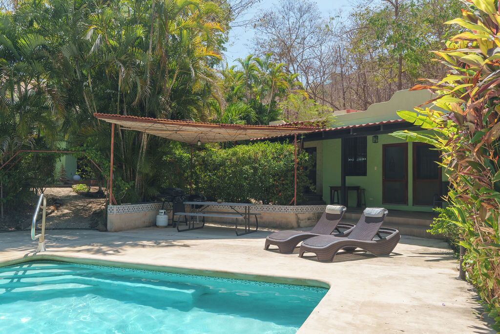 Ein Swimmingpool mit Liegestühlen, eine überdachte Terrasse und ein Gebäude mit grüner Fassade.
