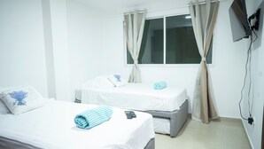 Une chambre d’hôtel avec deux lits, une fenêtre avec des rideaux, un téléviseur fixé au mur et une prise électrique.