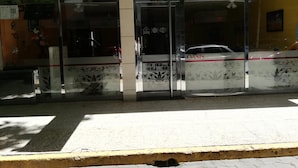 A building facade with large glass doors, a visible car, and a yellow curb. - Oasis (Mar del Plata)