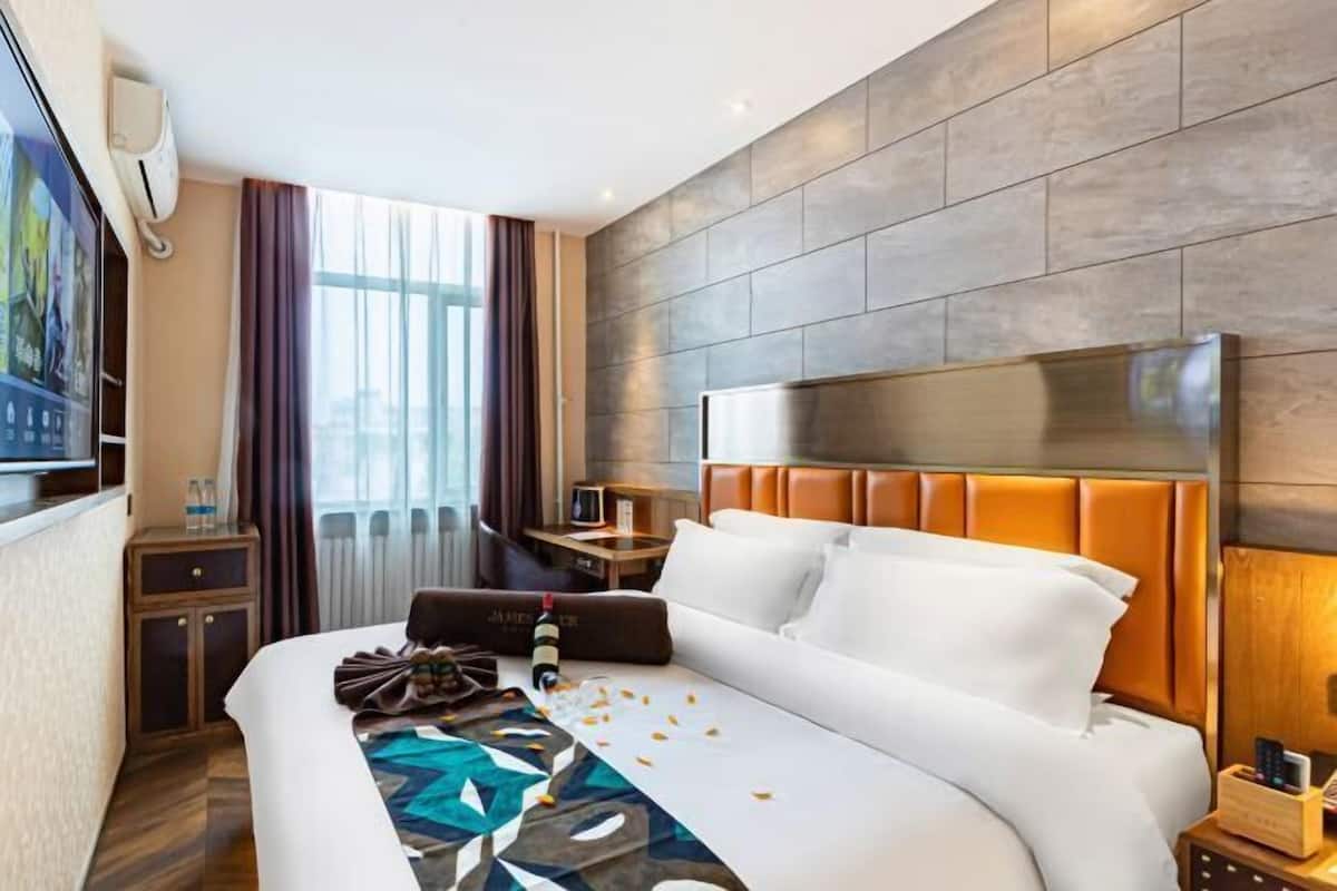 Ein Hotelzimmer mit einem großen Bett, einem Nachttisch, einem Fernseher und einem Fenster mit Vorhängen.