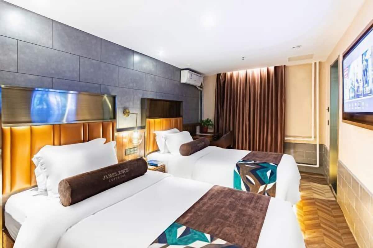 Ein Hotelzimmer mit zwei Betten, einem Fernseher, einer Wand-Klimaanlage und einem großen Fenster mit Vorhängen.