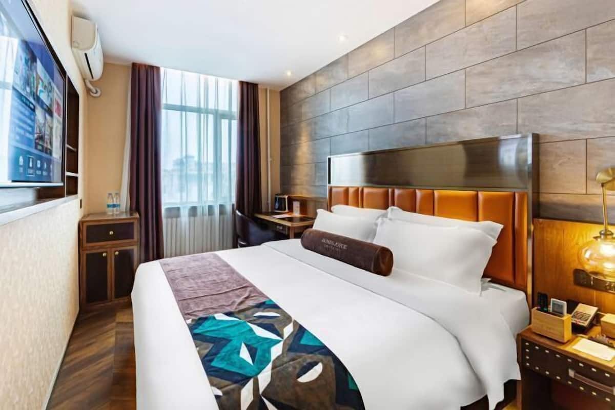 Ein Hotelzimmer mit einem großen Bett, einem Fernseher, einem Schreibtisch und einem Fenster mit Vorhängen.