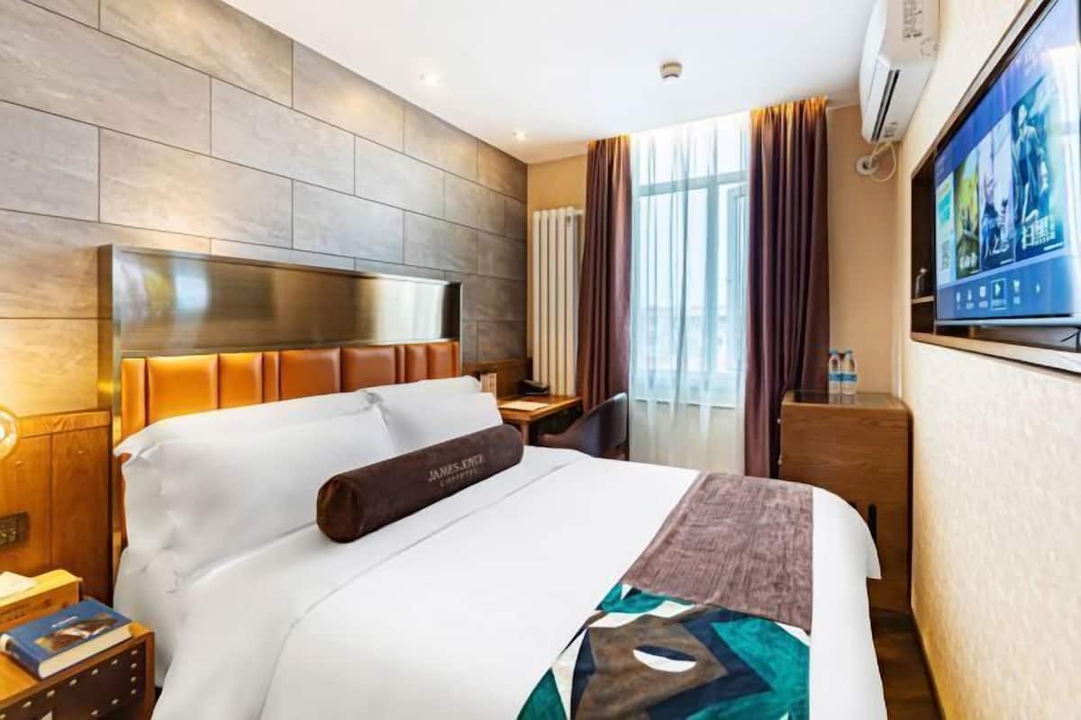Ein Hotelzimmer mit einem großen Bett, einem Flachbildfernseher, einem Nachttisch aus Holz und einem Vorhangfenster.