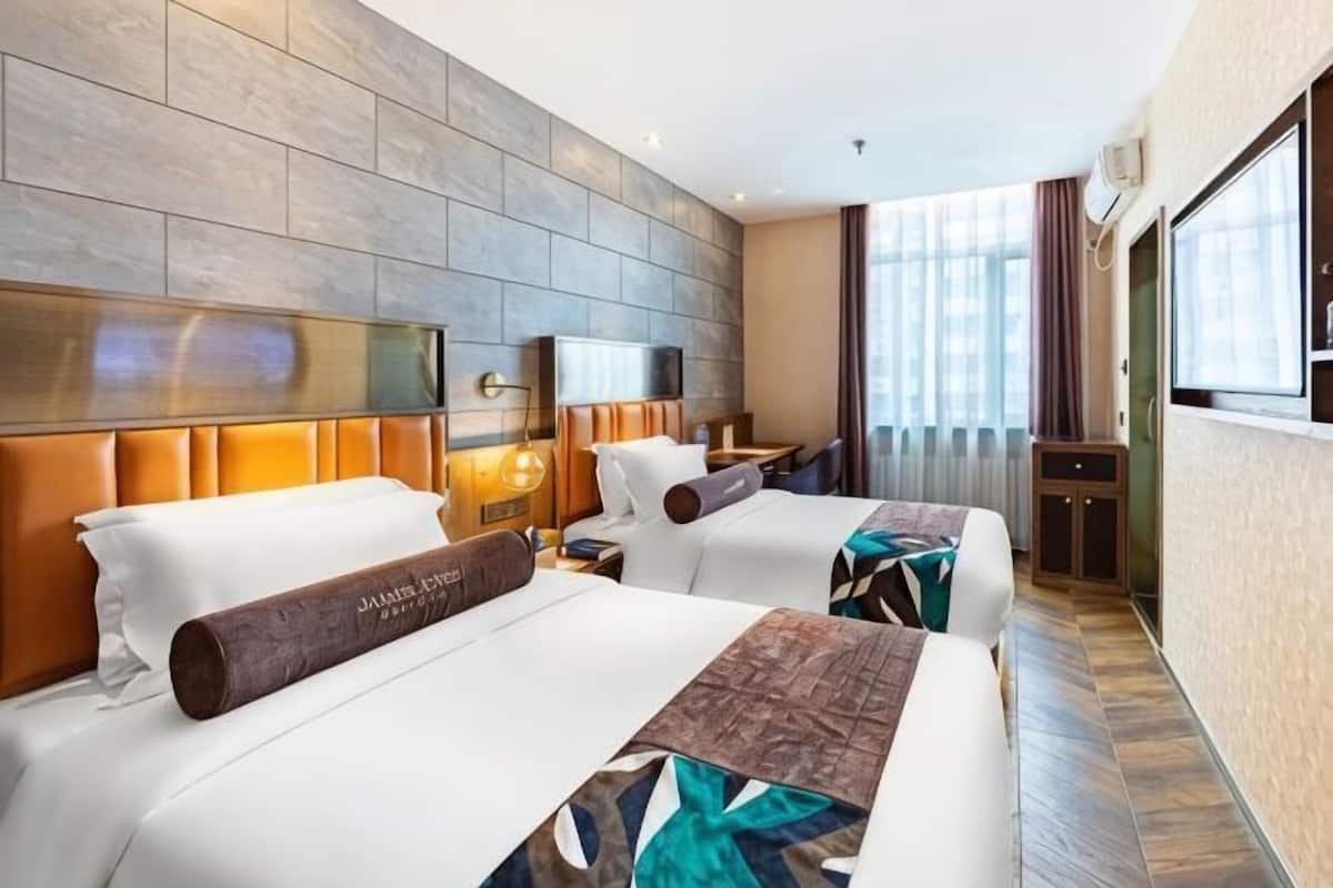 Ein Hotelzimmer mit zwei Betten, einem Fernseher, einem Schreibtisch und einem großen Fenster.