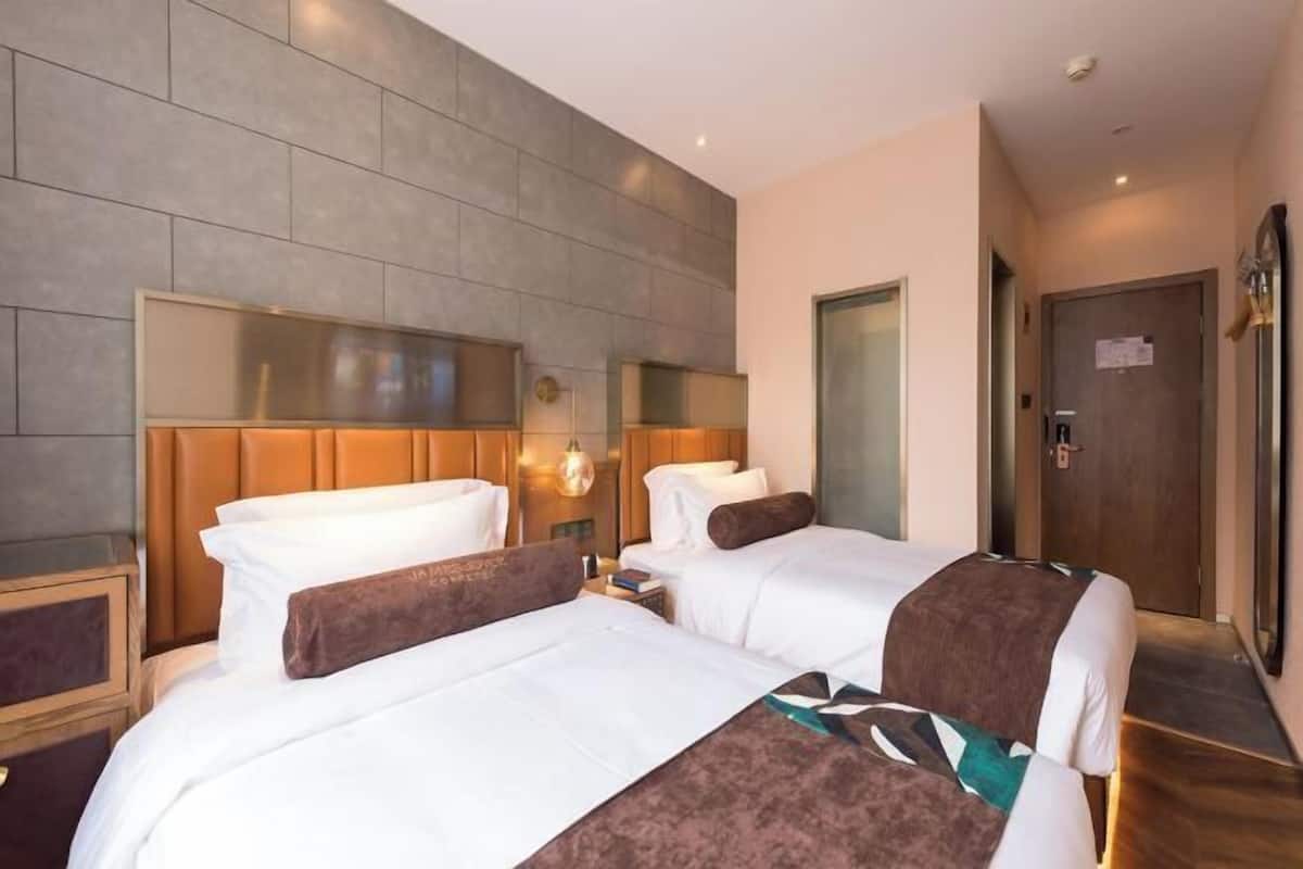 Ein Hotelzimmer mit zwei Betten, einem großen Spiegel, einem Holz-Kopfteil, einem Nachttisch und einer Tür.