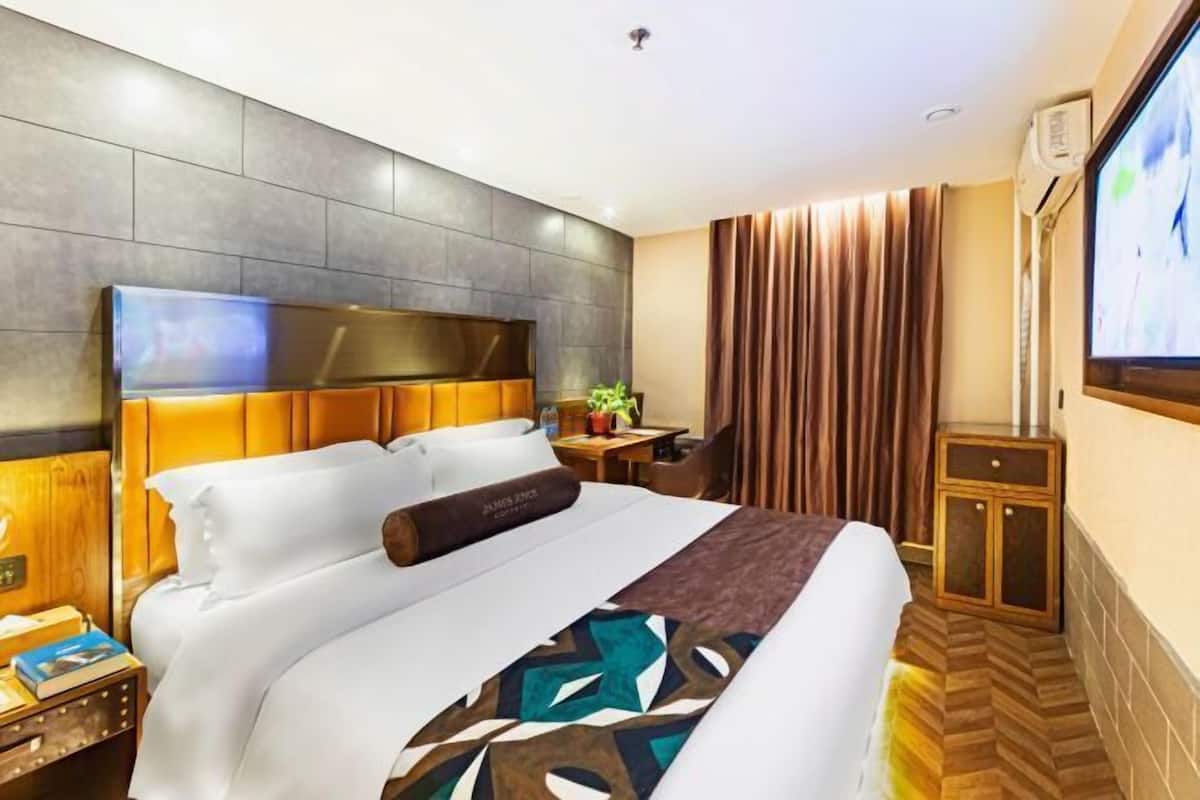 Ein Hotelzimmer mit einem großen Bett, einem Flachbildfernseher, einem Schreibtisch mit Stuhl und einem kleinen Schrank.
