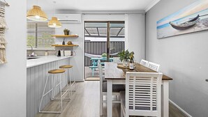 A modern kitchen with bar stools, a dining table with chairs, and a view of the outdoor patio. - Coastal convenience - 2 min walk to shops & cafes (Scarborough)
