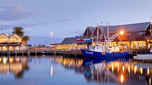 A waterfront marina with a docked boat, buildings with illuminated signs, and calm water reflecting the scene. - Coastal convenience - 2 min walk to shops & cafes (Scarborough)