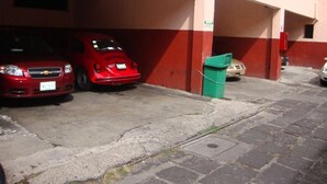 A parking area with two red cars parked under a building with red and white walls. - Hotel Virreyes (Puebla)