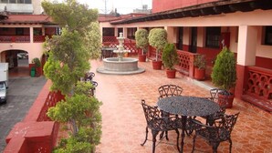 A courtyard with a fountain, potted plants, and outdoor seating. - Hotel Virreyes (Puebla)