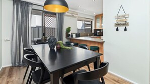 A modern dining area with a black table and chairs, a pendant light, and a kitchen in the background. - Coastal Elegance! A Luxurious, Dreamy Escape! (Scarborough)