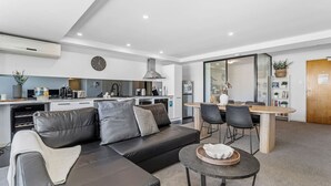 Um espaço de estar moderno com um sofá de couro preto, uma mesa de centro redonda e um espaço de refeições com mesa e cadeiras de madeira.