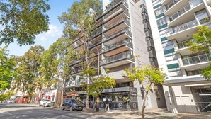 Um edifício residencial de vários andares com varandas, um restaurante no andar térreo e árvores em primeiro plano.