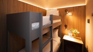 Habitación con literas, una pared de madera, una mesita de noche con un florero y una lámpara de pared.