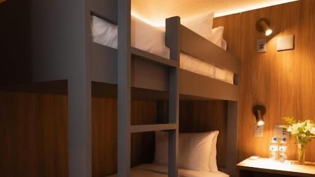 Dormitorio con literas, pared de madera, un escritorio pequeño con lámpara y un florero.