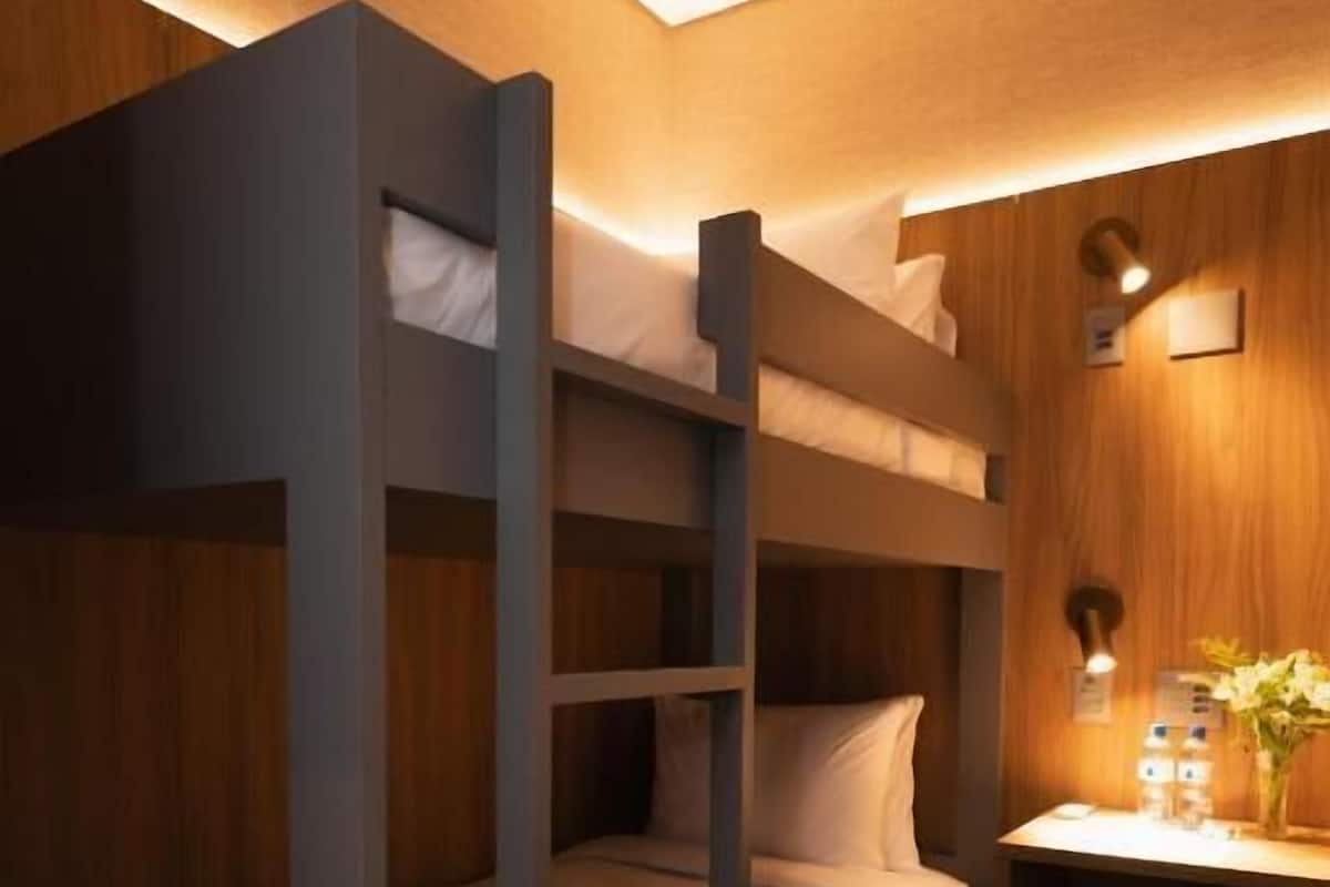 A bunk bed room with a wooden wall and a small desk with a lamp and a vase.