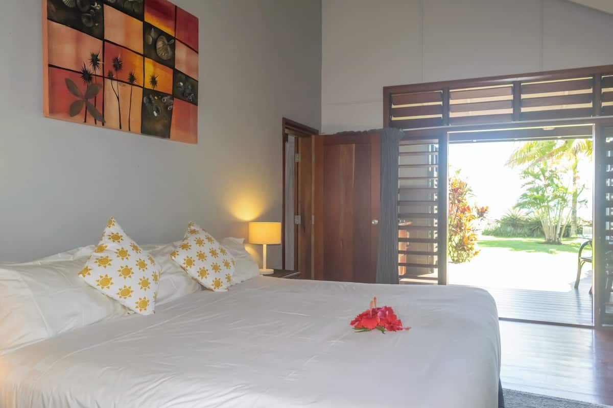 A hotel room with a large bed, a painting on the wall, and a view of the outdoors through an open door.