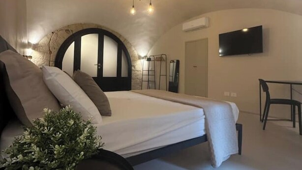 A bedroom with a large bed, a desk, a chair, a TV, and a unique arched ceiling.