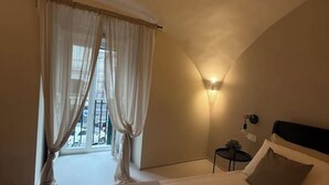 A bedroom with a bed, a nightstand, a wall-mounted lamp, and a window with curtains.