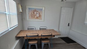 Ein Essbereich mit einem Holztisch, vier Stühlen, einem gerahmten Bild an der Wand und einer Tür mit Fußmatte.