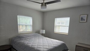 Ein Schlafzimmer mit einem Bett, zwei Fenstern, einem Deckenventilator, einem Nachttisch und einer Kommode.