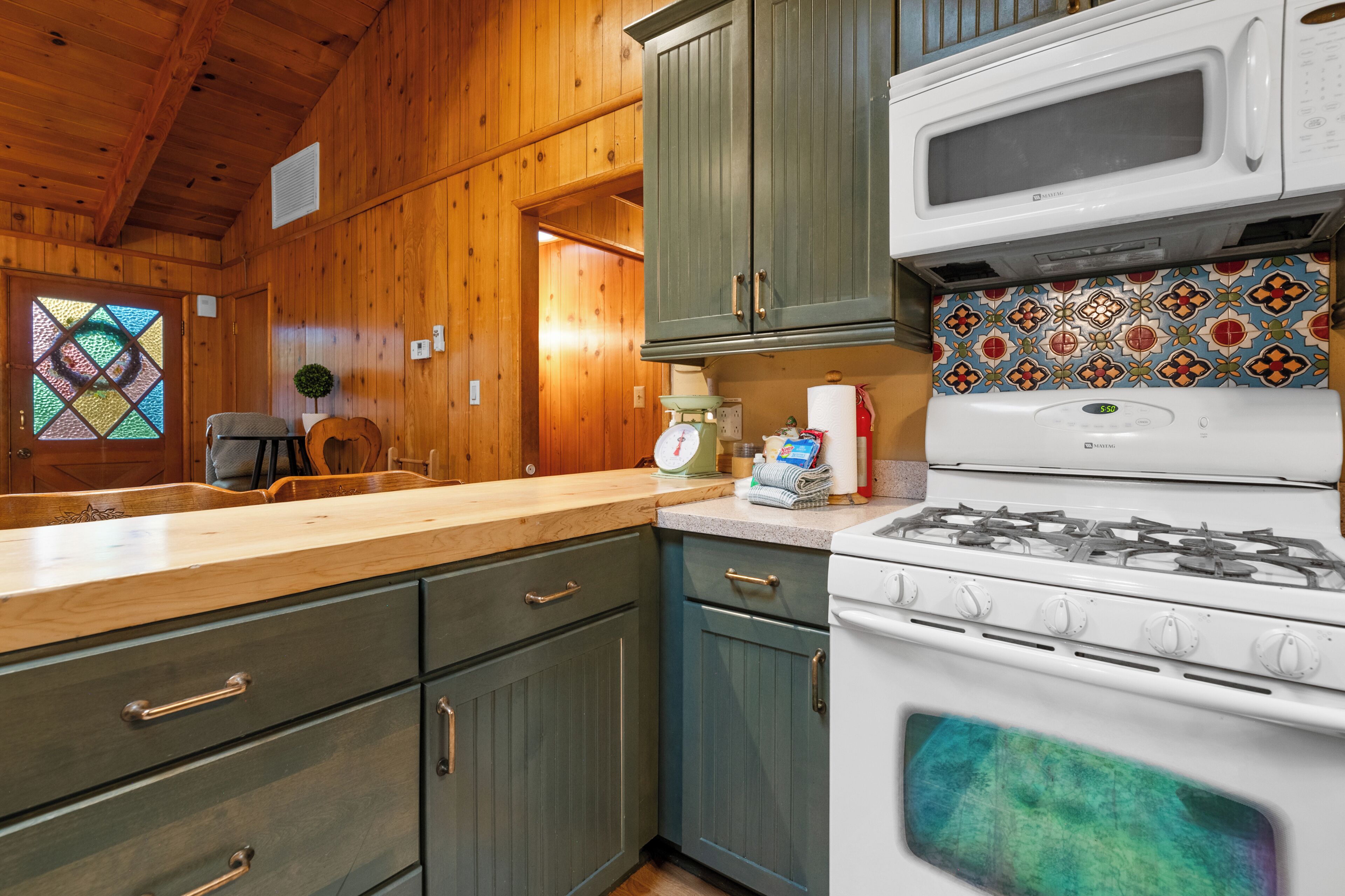 A kitchen with wooden cabinets, a stove, a microwave, and a window with a stained glass design.