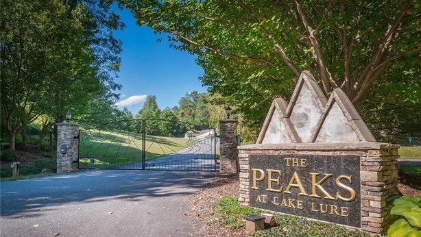 Un panneau indiquant « The Peaks at Lake Lure », avec une base en pierre et une partie supérieure en métal, entouré d’arbres et se dressant sous un ciel dégagé.