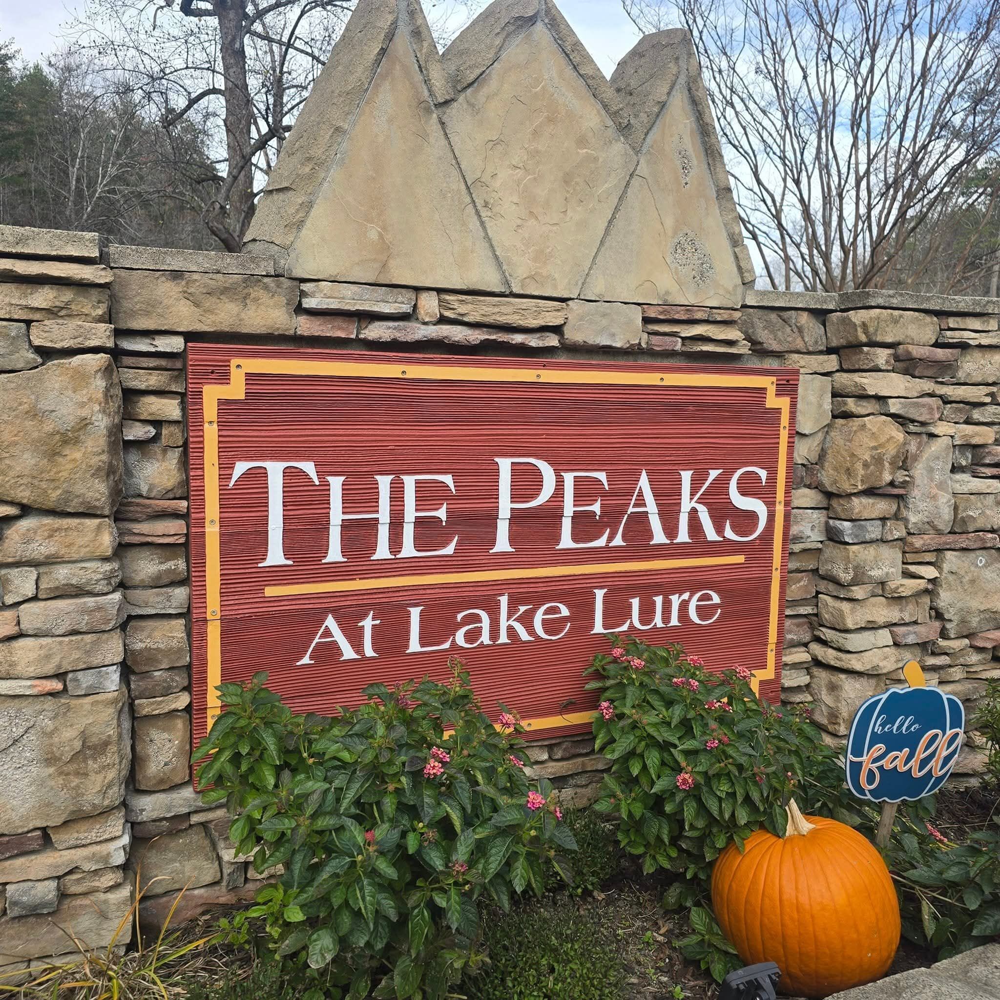 A sign for "The Peaks at Lake Lure" with a stone wall and a pumpkin.