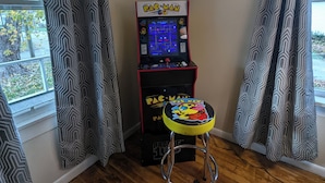 Habitació d'angle amb una màquina recreativa de Pac-Man, un tamboret petit i cortines amb dibuixos.