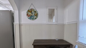 Zona de menjador amb taula de fusta i una cadira gris, un plat decoratiu a la paret i una finestra amb persianes.