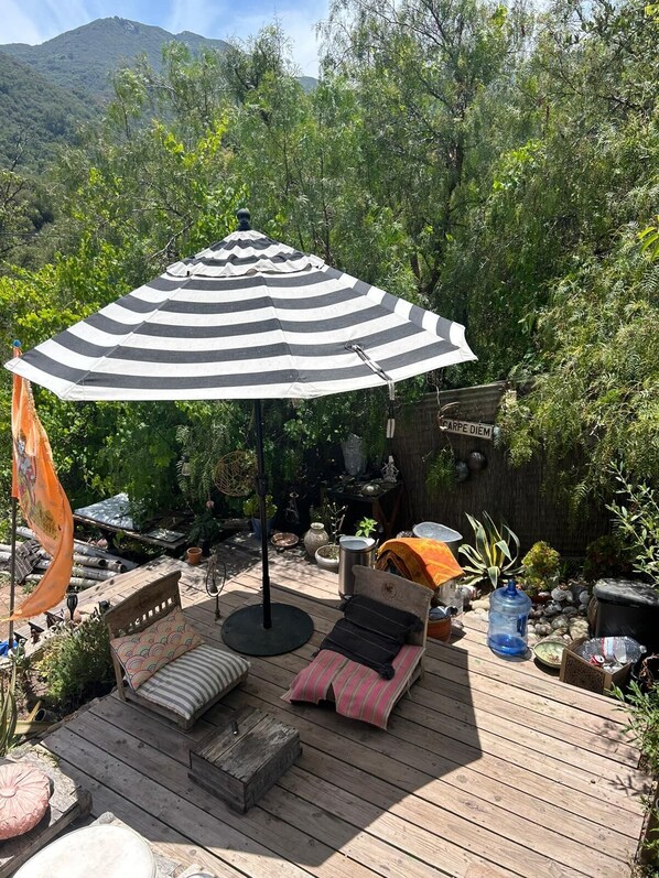 A wooden deck with a striped umbrella, a sofa, and a small table. - The Loft at Topanga Canyon: Cottage Retreat with Trails, Creek & Mountain View (Topanga)