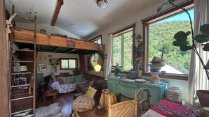 A cozy, rustic room with a loft bed, wooden furniture, and a view of greenery outside. - The Loft at Topanga Canyon: Cottage Retreat with Trails, Creek & Mountain View (Topanga)