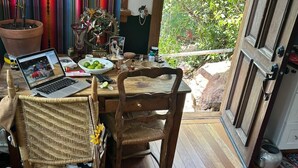 A dining area with a laptop on the table, wicker chairs, a potted plant, and a view of greenery outside. - The Loft at Topanga Canyon: Cottage Retreat with Trails, Creek & Mountain View (Topanga)