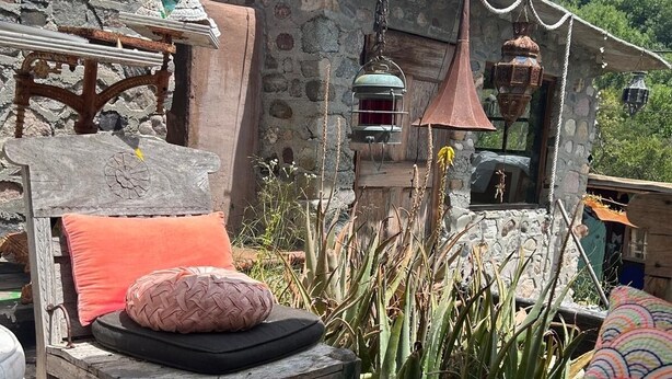 A rustic outdoor seating area with a wooden bench, cushions, and a rustic lantern. - The Loft at Topanga Canyon: Cottage Retreat with Trails, Creek & Mountain View (Topanga)