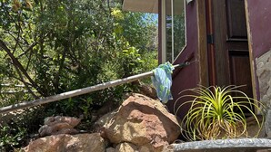 A stone wall with a large rock formation, a potted plant, and a metal chair. - The Loft at Topanga Canyon: Cottage Retreat with Trails, Creek & Mountain View (Topanga)