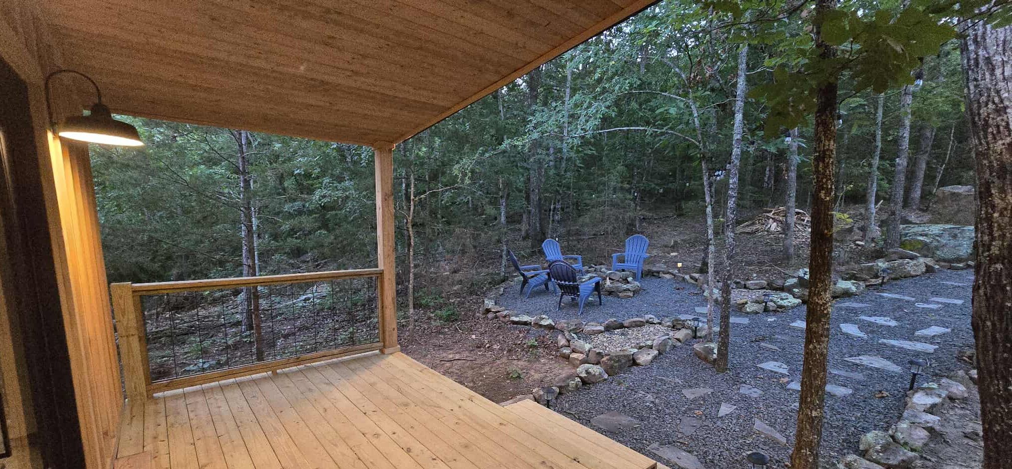 Um deck de madeira com guarda-corpo, com vista para uma área arborizada e um espaço de estar com cadeiras e lareira.