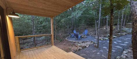 Um deck de madeira com guarda-corpo, com vista para uma área arborizada e um espaço de estar com cadeiras e lareira.