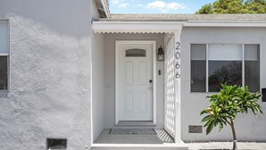 A house with a white exterior, a front door, and a small tree in the front yard. - Modern Coastal Retreat – 3BR Gem in Long Beach (Long Beach)