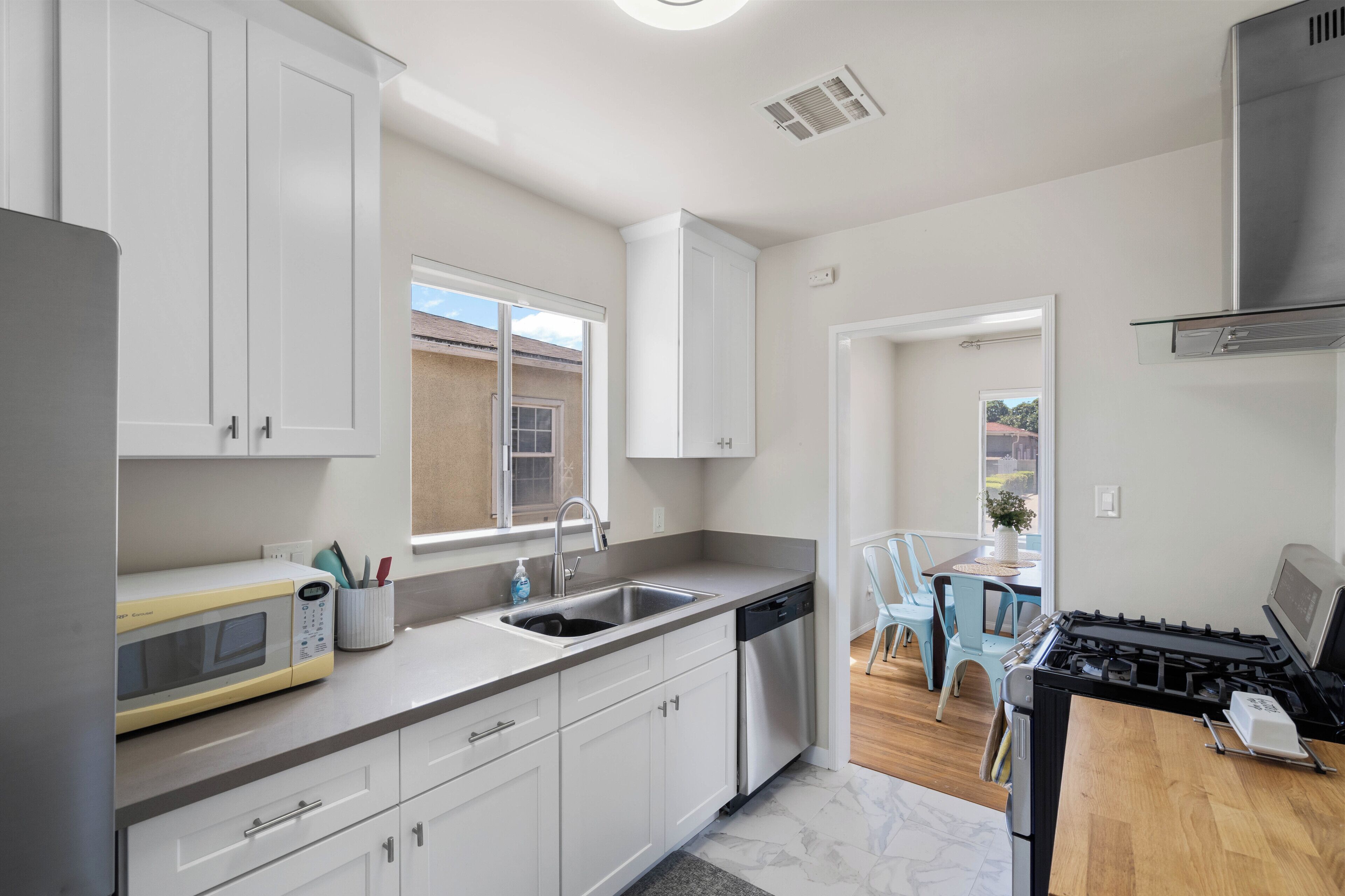 A modern kitchen with white cabinets, a microwave, a sink, and a stove.