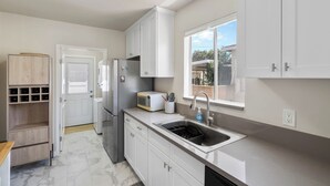 A modern kitchen with white cabinetry, a built-in microwave, a sink, and a window overlooking a backyard. - Modern Coastal Retreat – 3BR Gem in Long Beach (Long Beach)