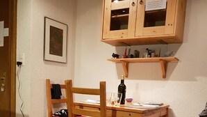 A small dining area with a wooden table and chairs, a cabinet above, and a power outlet on the wall.