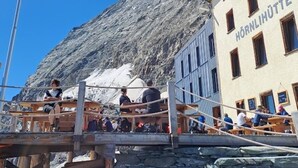A mountain view with a flag, a building labeled "Hörnihuette 35", and people sitting at tables.