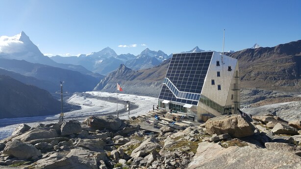 A modern building with a unique geometric design, situated in a mountainous area with a glacier in the background.