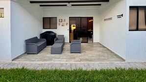 A covered patio area with grey outdoor furniture, a covered grill, and a sliding glass door leading to an interior dining area. - Beautiful house in the most exclusive área of San Miguel (San Miguel)