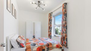 Ein Schlafzimmer mit einem Bett, einem Kleiderschrank, einem Fenster mit Vorhängen und einer Deckenleuchte.