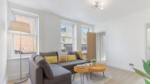 Ein modernes Wohnzimmer mit einem Ecksofa, einer Stehlampe und einem kleinen runden Tisch.