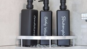 Drei schwarze Flaschen mit Conditioner, Duschgel und Shampoo auf einem Metallregal.