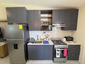 Eine moderne Küche mit grauen Schränken, einem Edelstahl-Kühlschrank, einer Mikrowelle, einem Herd und einem Spülbecken.